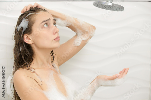 Puzzled foamed young woman after the water in the shower was turned off, looking up at the shower. Lifestyle
