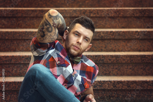 Young tattooed man posing on stairs, outdoor