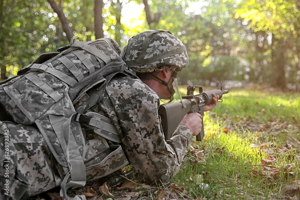Soldier taking aim from rifle in forest, close up view