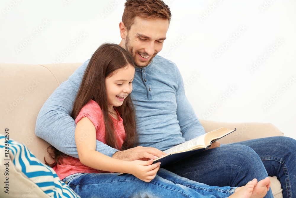 Father and daughter reading book on couch