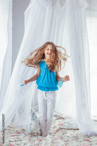 little cute girl in blue shirt jumping on bed © pyrozenko13