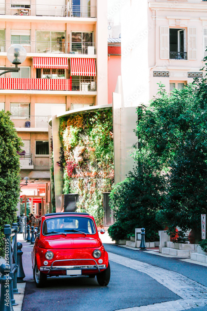 small red retro car parked on a narrow street European style overgrown with greenery