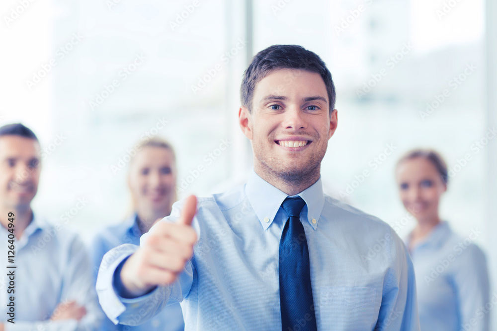 smiling businessman showing thumbs up in office smiling businessman showing thumbs up in office