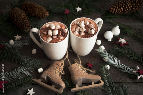 Two cups of hot cocoa or hot chocolate with marshmallows with fir tree and skates, traditional beverage for winter time. Christmas concept.