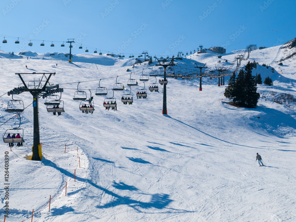 Ski lift and ski slope with skiers under it on sunny winter day with blue sky. Alpine resort Silvretta Arena near Samnaun and Ischgl, Switzerland and Austria, Alps, Europe