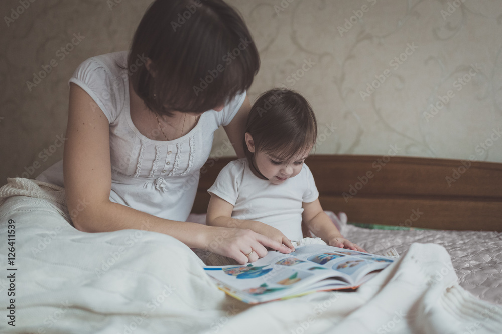 young mother and daughter Toddler reading book sitting on bed young mother and daughter Toddler reading book sitting on bed