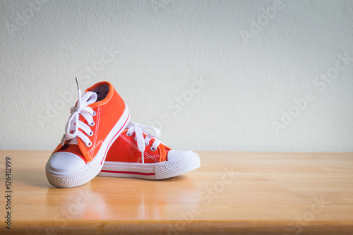 Baby sneakers on wooden table over wall grunge background, vintage style