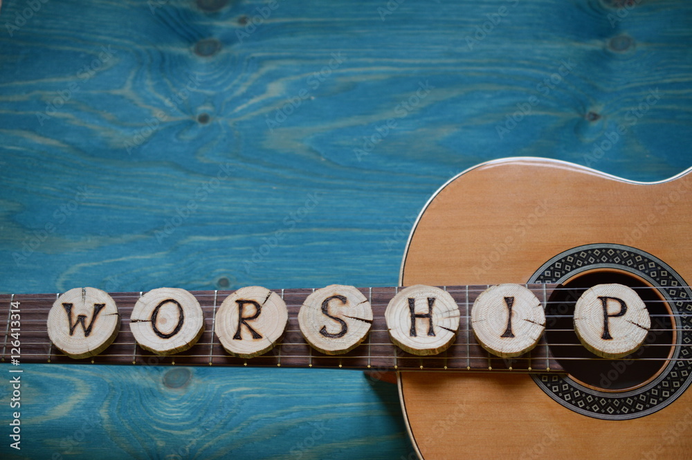 Fototapeta premium gitara na turkusowym drewnianym tle z drewnianymi kawałkami z napisem: WORSHIP