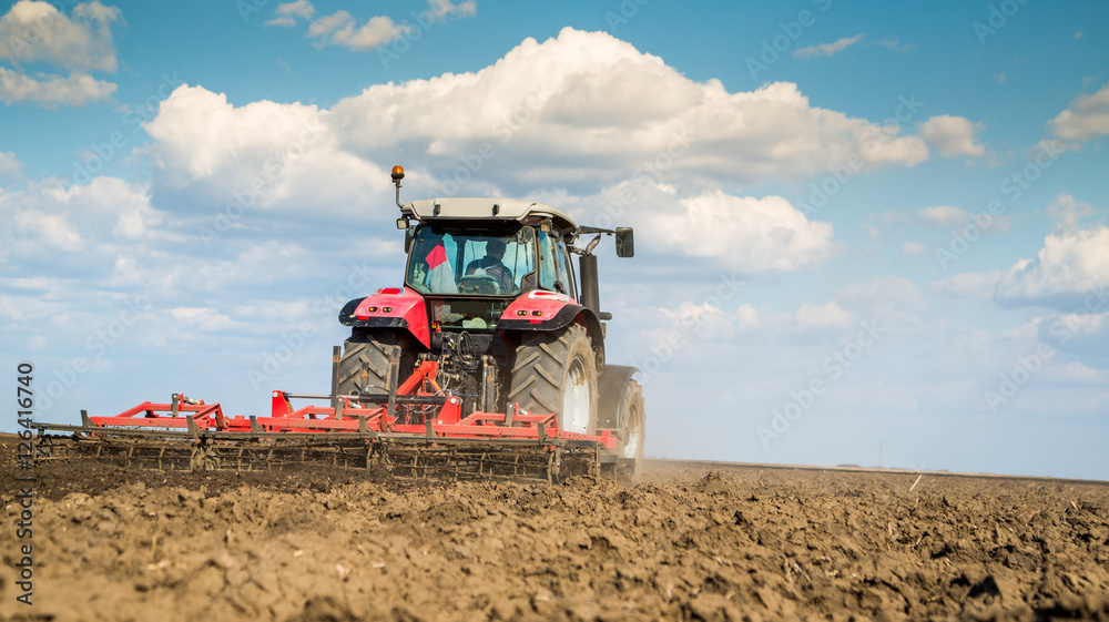 Fototapeta premium Farmer in tractor preparing land with seedbed cultivator
