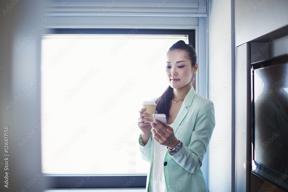 A business woman preparing for work, holding a cup of coffee and checking her smart phone. A business woman preparing for work, holding a cup of coffee and checking her smart phone.