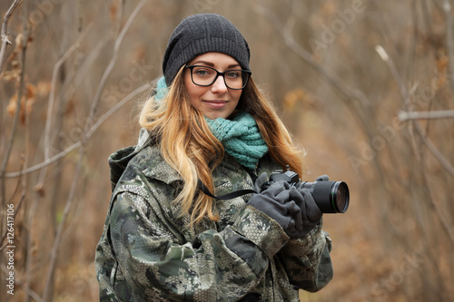 Young beautiful woman in camouflage outfit discovering nature in the forest with photo camera. Travel photography lifestyle concept.