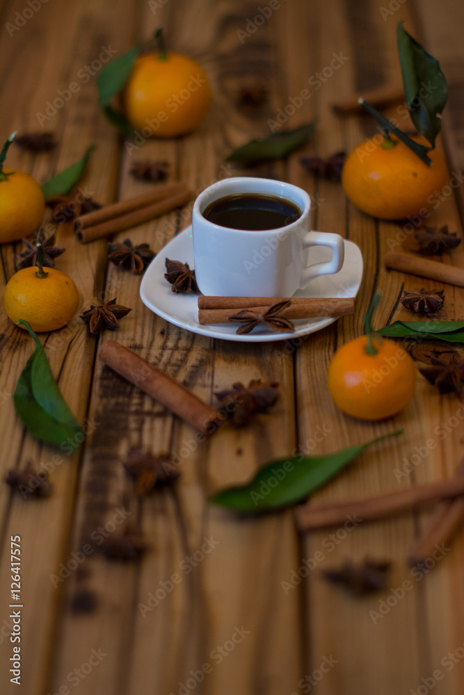 Small white cup of coffee, cinnamon sticks, star anise and mandarins on wooden background