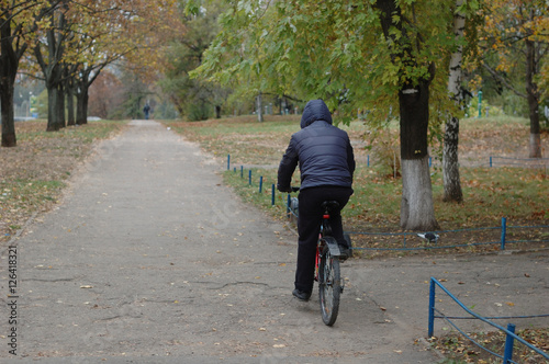 A man rides a bicycle in a park in autumn - rear view.