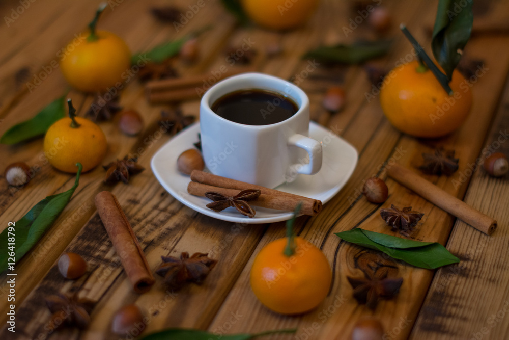 Small white cup of coffee, cinnamon sticks, star anise, hazelnuts and mandarins on wooden background Small white cup of coffee, cinnamon sticks, star anise, hazelnuts and mandarins on wooden background