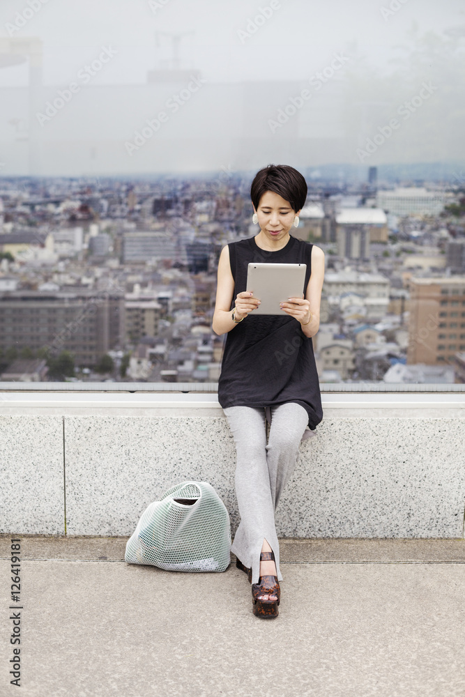 Woman using a digital tablet, with her back to the view over a large city. Woman using a digital tablet, with her back to the view over a large city.