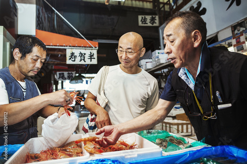 A traditional fresh fish market in Tokyo. Two people selecting shellfish for a customer to buy, filling a bag from boxes of prawns. photo