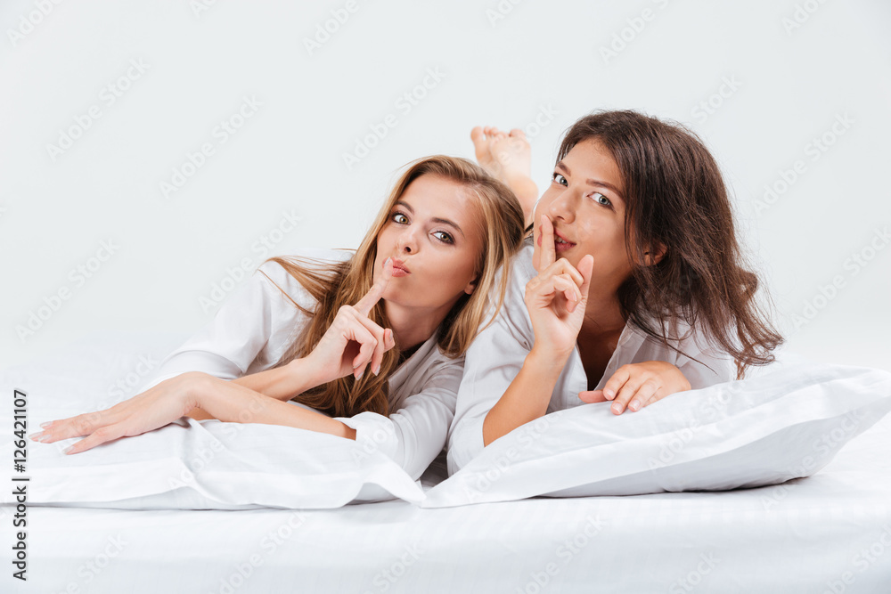 Women showing silence gesture and looking at camera with finger