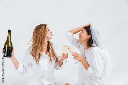 Two smiling women wearing bridal veil and holding champagne bottle