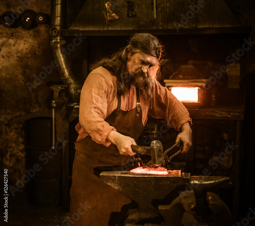 Senior blacksmith forging the molten metal on the anvil in smithy