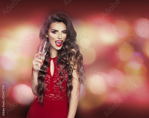 Sexy model girl with glass of champagne at party, drinking champagne over holiday glowing background. Beauty woman with perfect fashion makeup. Christmas and New Year holiday celebration.
