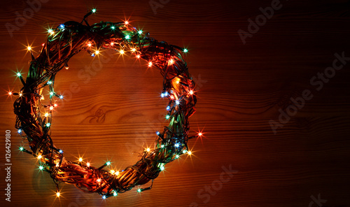 Happy New Year and Merry Christmas holiday template card with copyspace on dark old wooden background. Wreath and garlands of colored light bulbs. Circle place for price and space for shop sale item.