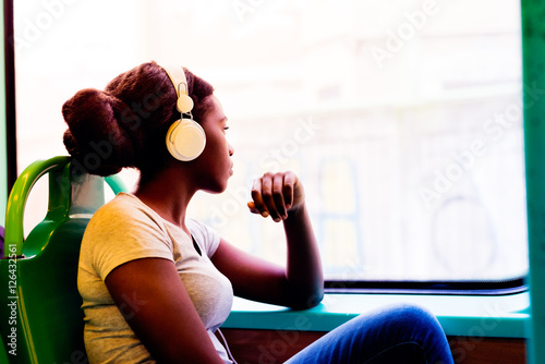 Young black woman listening music travelling by bus looking outdoor the window, pensive - thoughtful, thinking future, music concept