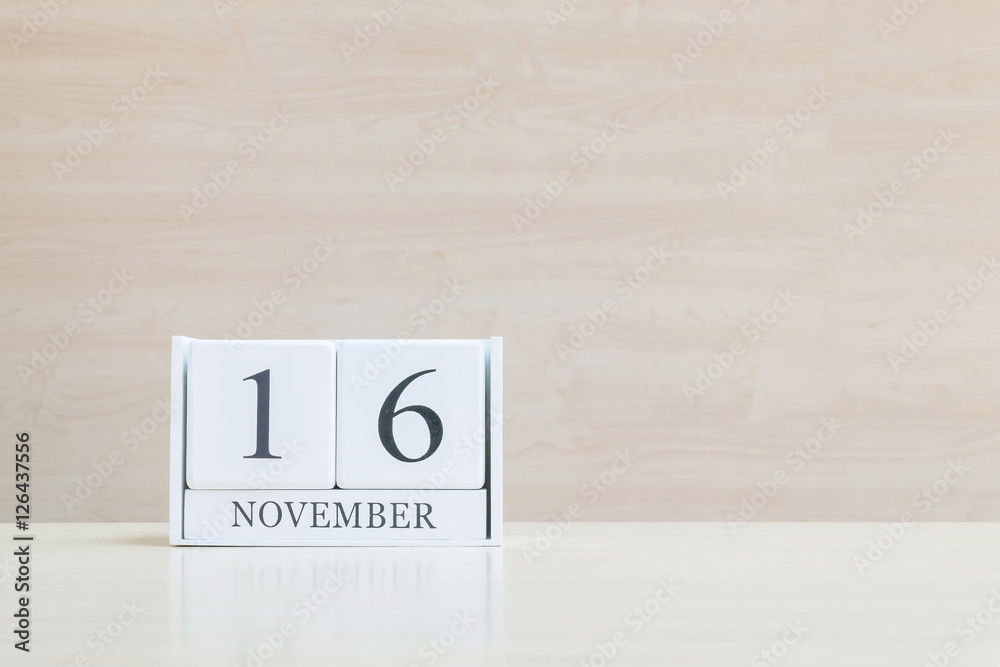 Closeup surface white wooden calendar with black 16 november word on blurred brown wood desk and wood wall textured background with copy space , selective focus at the calendar Closeup surface white wooden calendar with black 16 november word on blurred brown wood desk and wood wall textured background with copy space , selective focus at the calendar