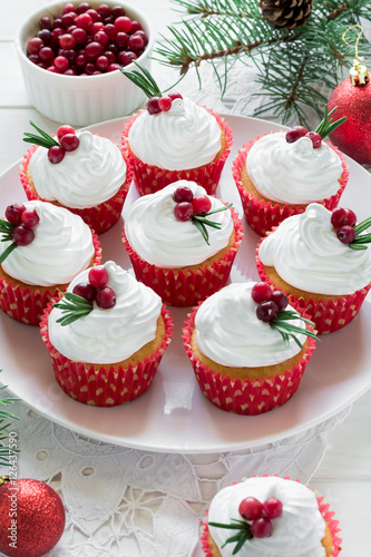 Christmas cupcakes with vanilla frosting  cranberries and rosemary on white wooden background. Selective focus