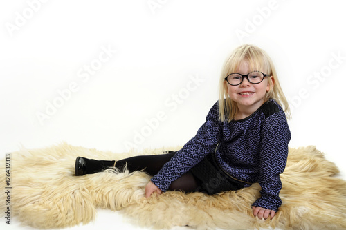Śliczna dziewczynka, blondynka siedzi na skórze z barana.