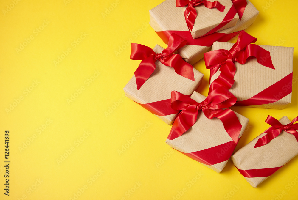 Christmas gifts wrapped in brown paper with red silk bows on a bright yellow background and blank space at side Christmas gifts wrapped in brown paper with red silk bows on a bright yellow background and blank space at side