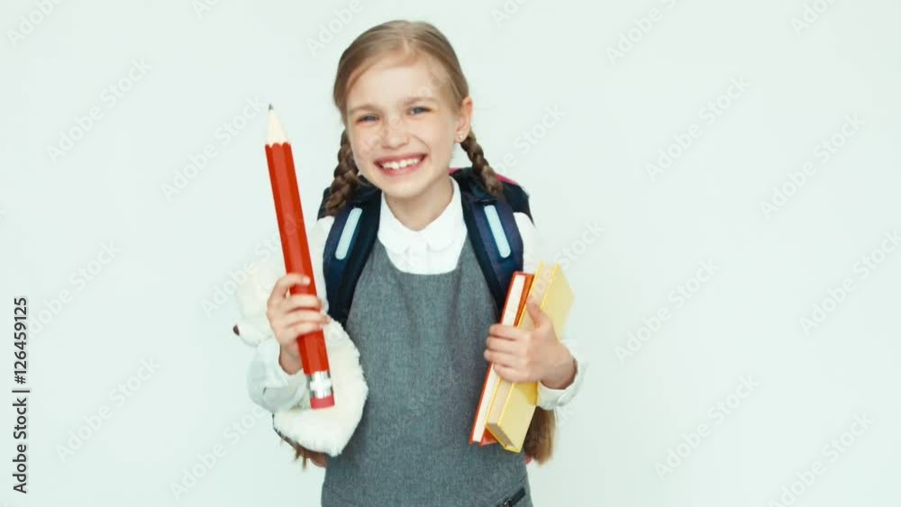 Cute schoolgirl 7-8 years with school knapsack holding books and big pencil and teddy bear and laughing at camera on white background Cute schoolgirl 7-8 years with school knapsack holding books and big pencil and teddy bear and laughing at camera on white background