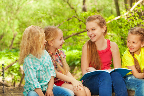Cute girl reading the book to her friends outdoor