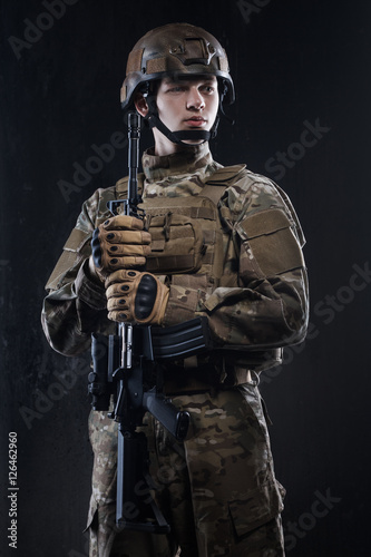 Man in military uniform with assault rifle on background of dark wall. Defender of his homeland.