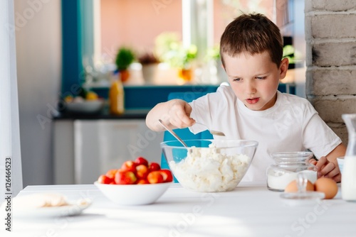 Boy adding sugar to white cheese in bowl for cheesecake.