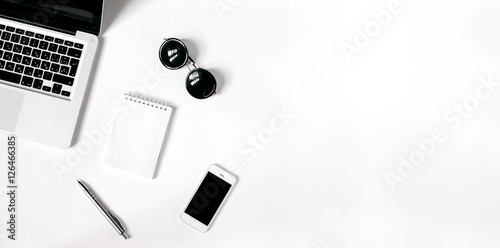 White office desk with laptop, smartphone, sunglasses and notebook . Top view with copy space, flat lay.