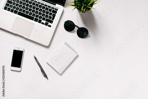 White office desk with laptop, smartphone, office plant and notebook . Top view with copy space, flat lay.