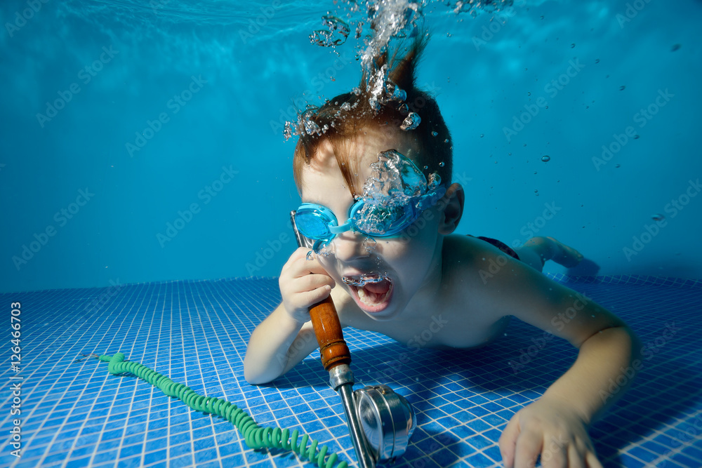 Little boy underwater in swimming pool lies at the bottom, holding a