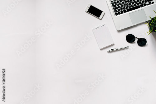 White office desk with laptop, smartphone, office plant and notebook . Top view with copy space, flat lay.
