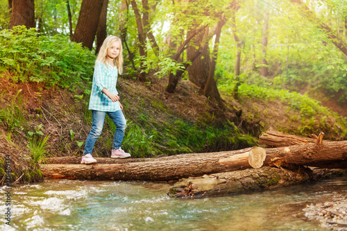 Little girl crossing log bridge in the forest