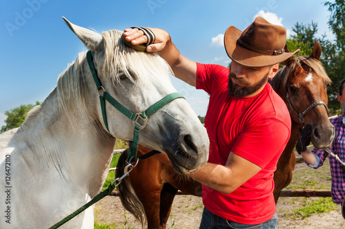 Man in cowboy hat grooming the mane of his horse