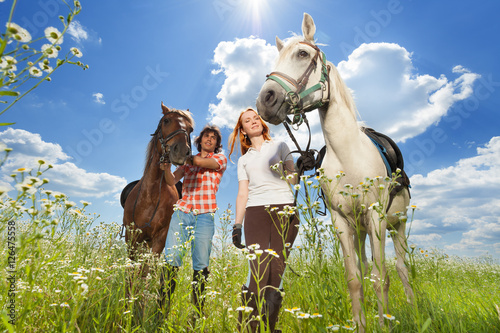 Young couple with horses walking in flowery meadow