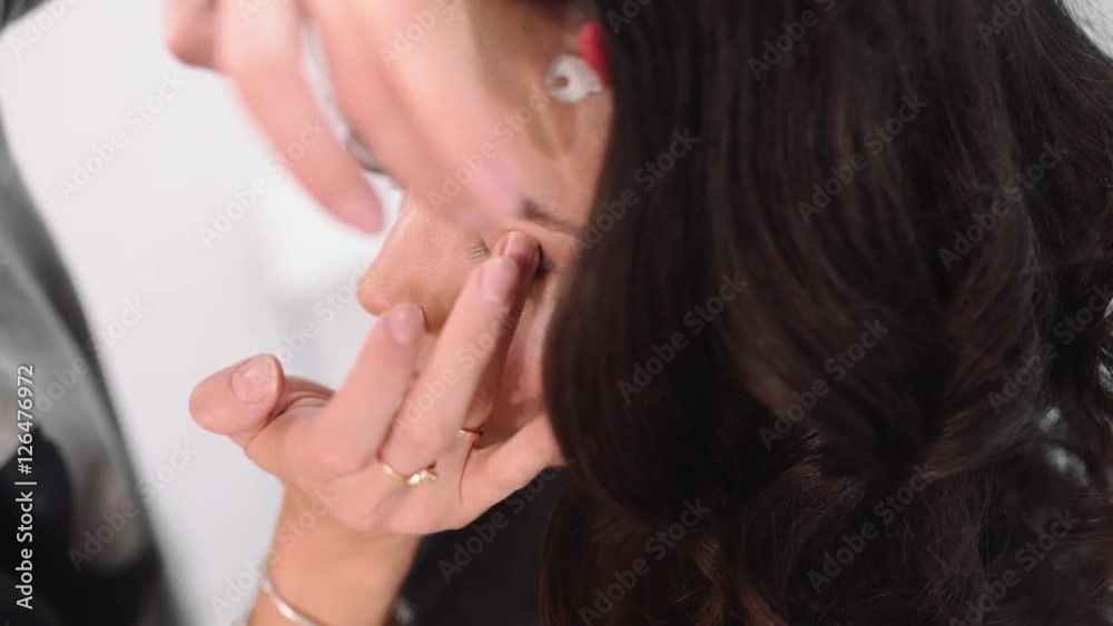 Makeup artist applies the tone to the skin, visagist makes make up for beautiful caucasian woman, white girl with pretty face at the beauty salon