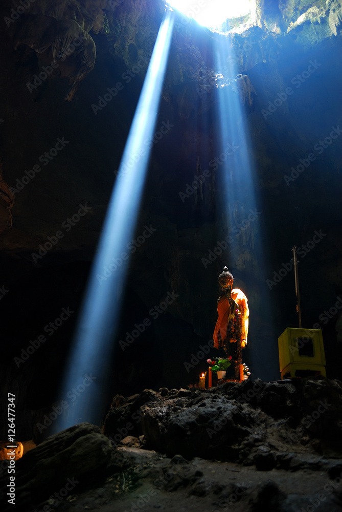 Fotka „A Buddha statue with the rays of light shining through the top of a  cave“ ze služby Stock | Adobe Stock