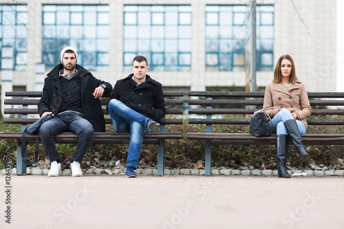 Group of friends sitting on a bench in park separately