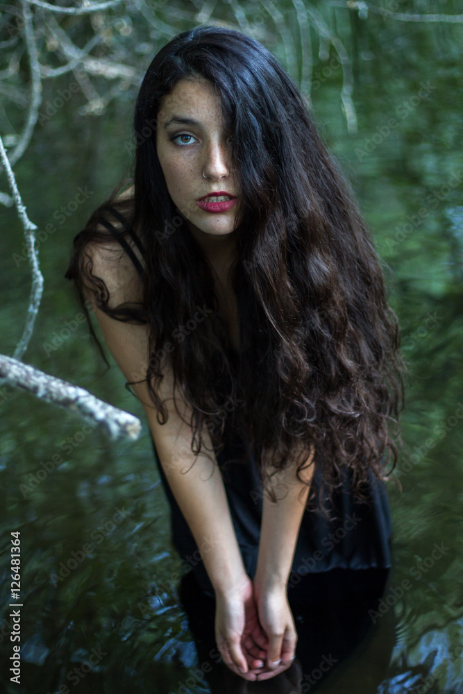 Pretty girl with black hair bathing in a lake of a pretty but sinister forest. She is wearing a black dress. Pretty girl with black hair bathing in a lake of a pretty but sinister forest. She is wearing a black dress.