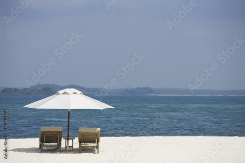 two lounge chairs on white sand beach