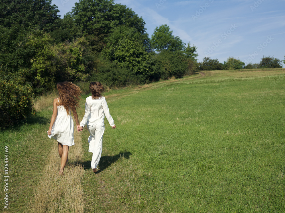 Two young women walking in field holding hands Two young women walking in field holding hands