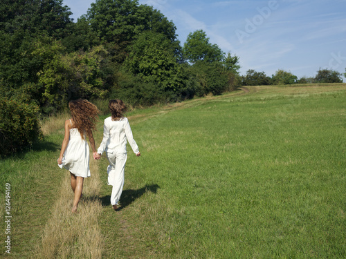 Two young women walking in field holding hands