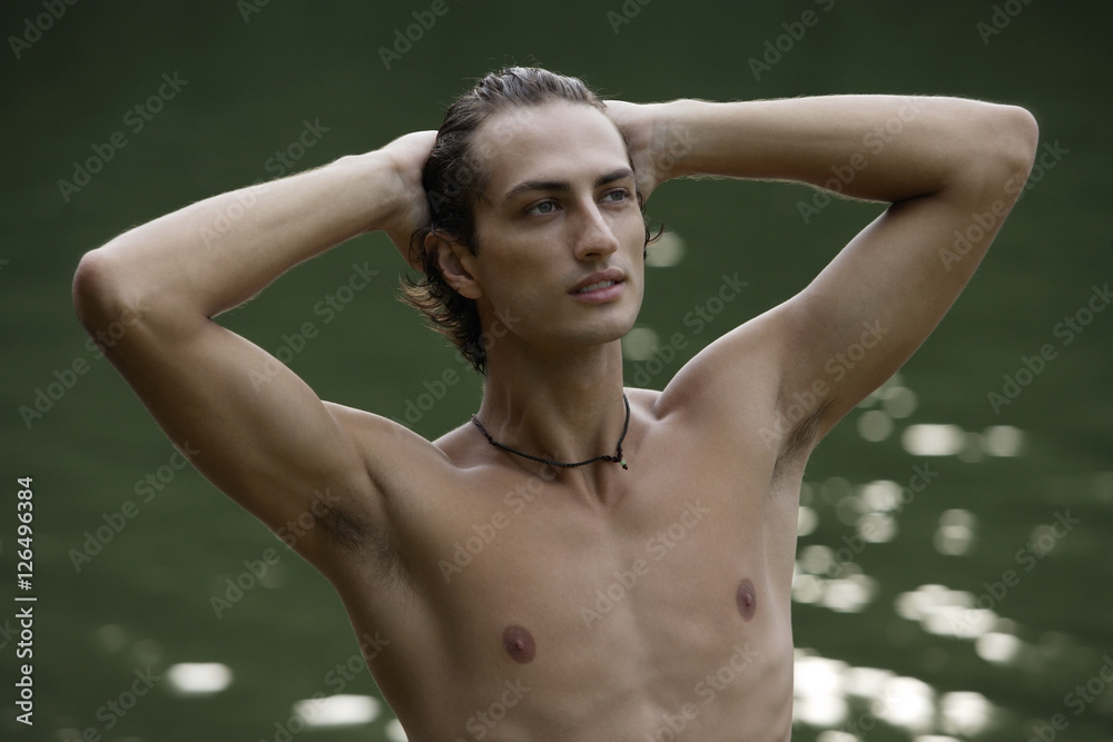 Young man standing in lake, hands on head