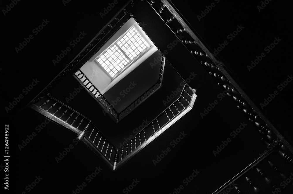 Obraz premium Outlines of the square staircase in building in low light with attic window. Bottom view